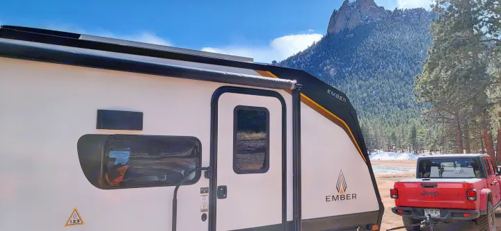 Explore nature: An Ember travel trailer (rv rental) with a red Jeep Gladiator, parked in a scenic mountain campsite.. Ember Overland 2023