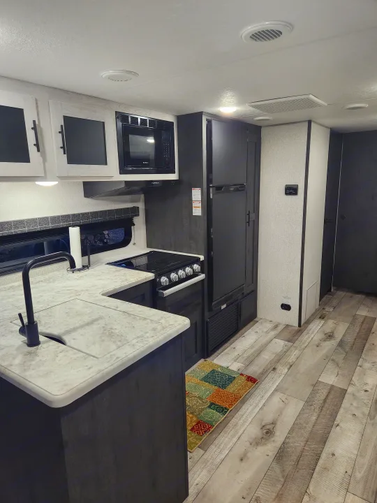 Modern RV rental kitchen with fridge, microwave, stove, and sink. Light and dark cabinetry, wood-look floor.. Sportsmen Other 2022