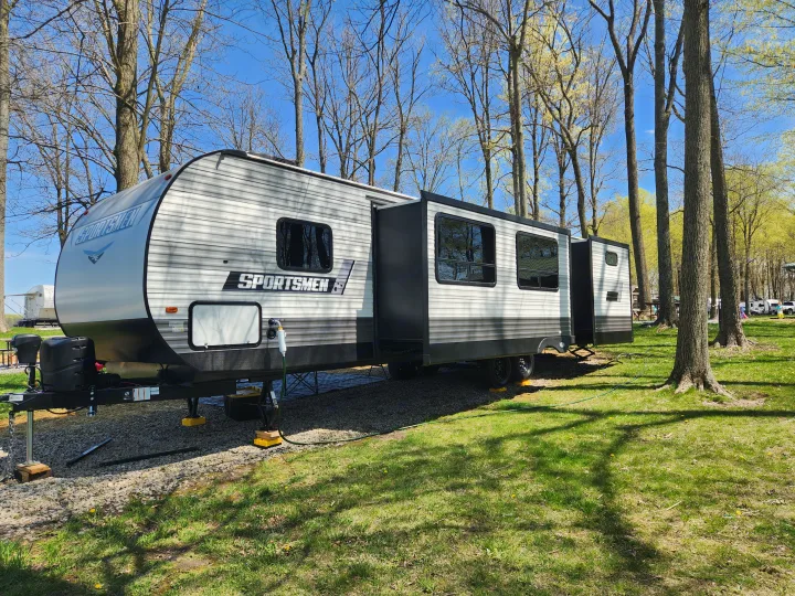 Enjoying nature in an RV rental travel trailer, parked on gravel with extended slide-outs in a wooded campsite.. Sportsmen Other 2022
