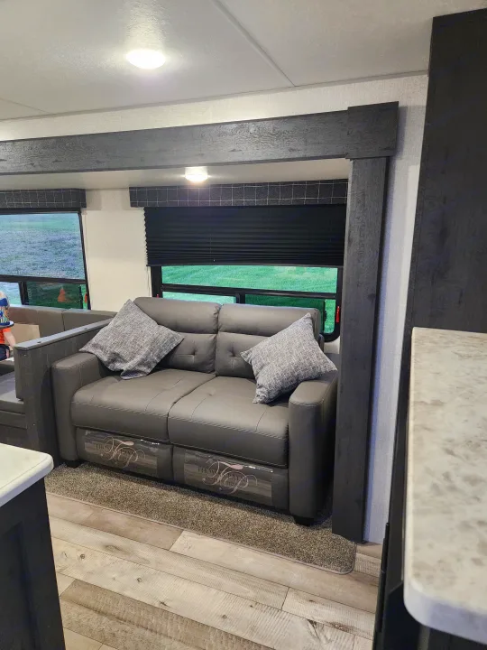 Spacious RV rental interior features a plush grey sofa, wood floor, and large windows for scenic views.. Sportsmen Other 2022