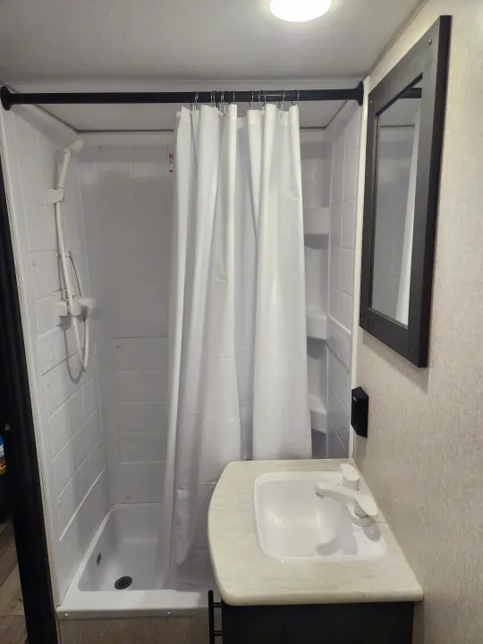 Inside an RV rental: Compact white bathroom with shower stall, curtain, sink, mirror, and overhead vent.. Sportsmen Other 2022