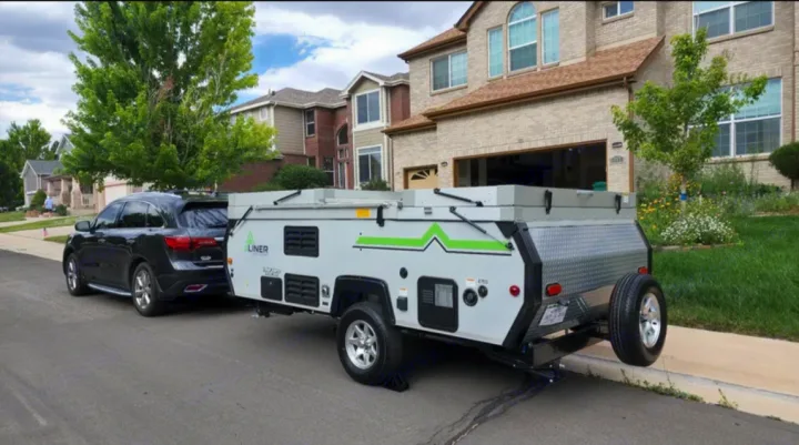 A sleek SUV tows a modern grey A-Liner pop-up RV rental, parked on a residential street. Perfect for your next trip!. A-liner Classic 2022
