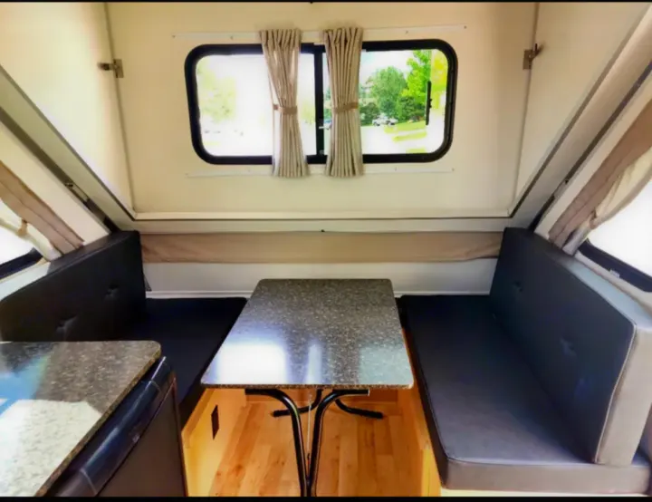 Inside this rv rental: a cozy dinette with black benches, a table, and bright windows. Perfect compact camper interior.. A-liner Classic 2022