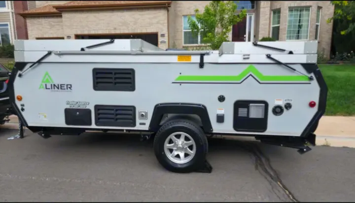 Light gray A-liner A-frame pop-up camper, seen in front of a house, ideal for your next RV rental trip.. A-liner Classic 2022