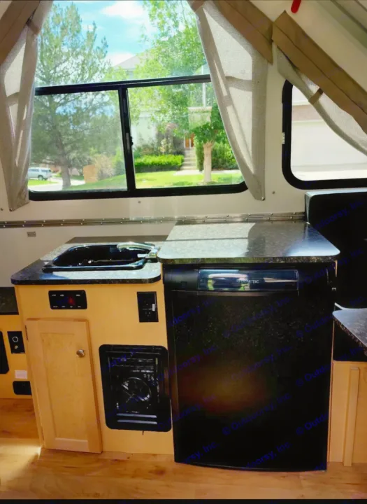 Compact RV rental kitchenette featuring a sink, stove, and refrigerator, with a bright view of the outdoors.. A-liner Classic 2022
