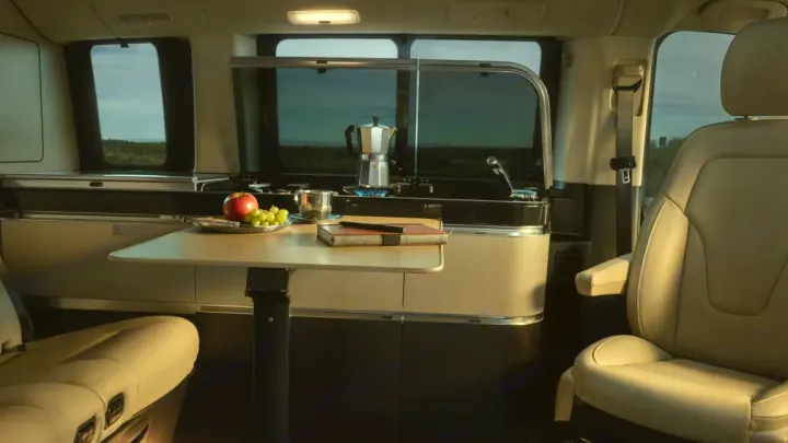 Experience comfort in this RV rental! Interior features a compact kitchen with a brewing coffee pot, dining table with fruit, and cozy seating.. Mercedes Class V Marco Polo 2023