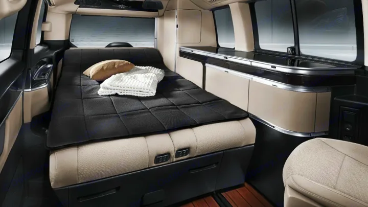 An rv rental camper van interior, showing a made bed with a black mattress pad, pillows, and a built-in kitchenette.. Mercedes Class V Marco Polo 2023