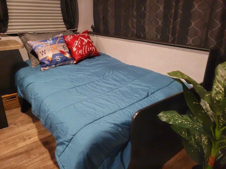 Comfortable RV rental bed with a blue comforter, "cottage is calling" pillow, and rustic decor. Ideal for your next trip.. Forest River Cherokee Grey Wolf 2022