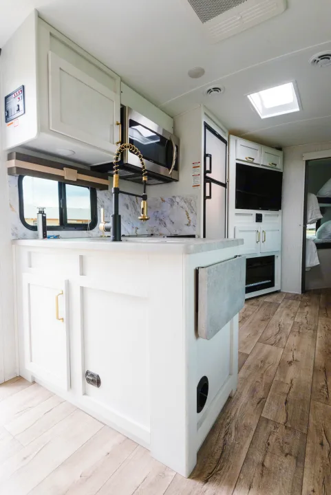 Modern RV rental kitchen with white cabinets, gold accents, and wood flooring. Ideal for comfortable travel.. Dutchmen Astoria 2022