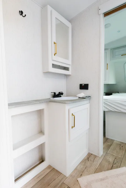 Clean white bathroom vanity in an RV rental, featuring a sink, mirror cabinet, and open shelving.. Dutchmen Astoria 2022