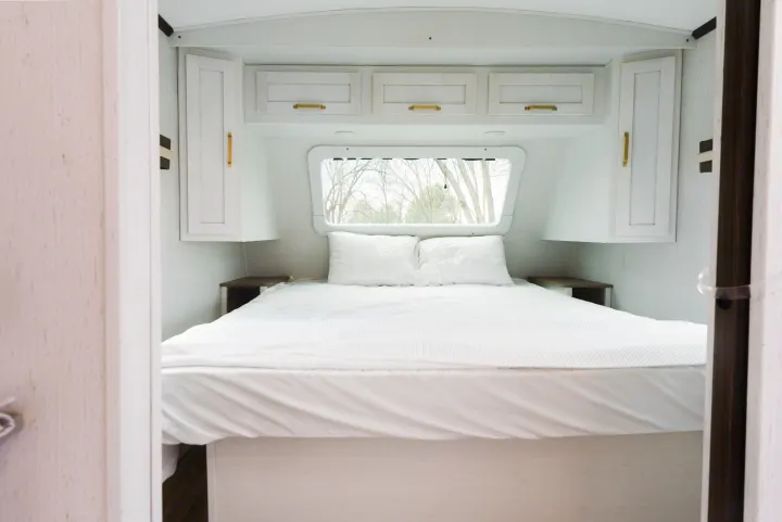 White and bright RV rental bedroom featuring a comfy bed, modern cabinets, and a large window view.. Dutchmen Astoria 2022