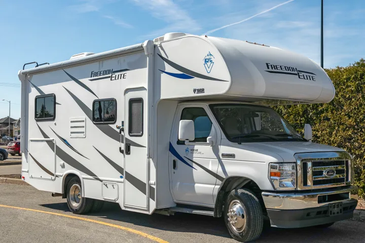 A white Class C motorhome (Freedom Elite RV rental) is parked outdoors on a sunny day.. Thor Freedom Elite 2021