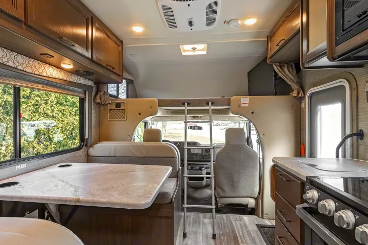 Explore this cozy RV rental interior: dining area, kitchen, and cab-over bunk. Ideal for family road trips.. Thor Freedom Elite 2021