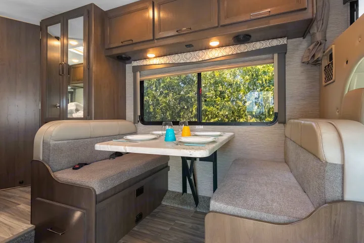 Cozy RV rental dinette: a table with place settings, comfortable benches, & a window view of trees.. Thor Freedom Elite 2021