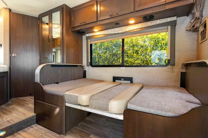Spacious RV rental interior with a convertible dinette bed, wood-look cabinetry, and a large window offering nature views.. Thor Freedom Elite 2021
