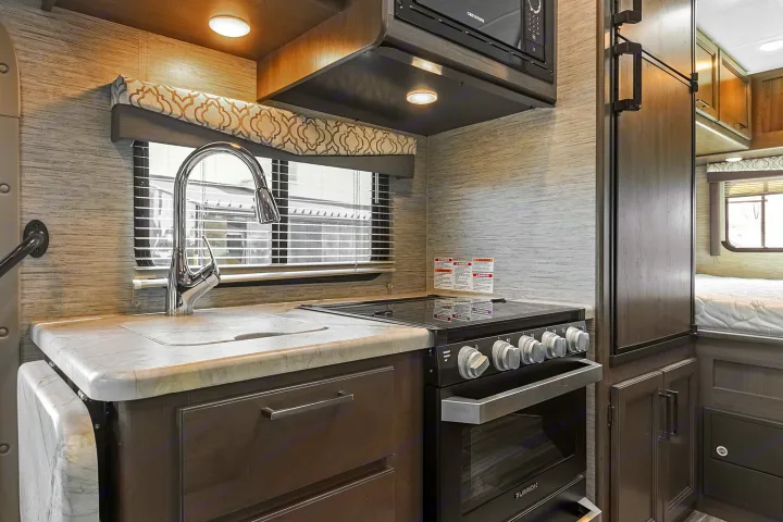 Inside an RV rental: compact kitchen featuring a bright sink area, stove, microwave, and refrigerator for road trips.. Thor Freedom Elite 2021