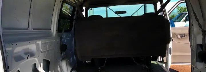 View of a white van's interior, showing bare walls and a dark bench seat, ideal for an RV rental.. Ford E-150 2000