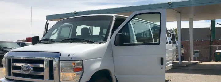 White Ford van for RV rental, driver's door open, parked under a canopy with other rental vehicles.. Ford E-350 2009
