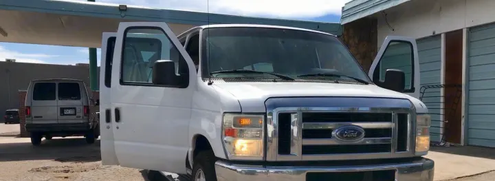 White Ford van with open doors parked near a grey van and storage units. Great for moving or an RV rental alternative.. Ford E-350 2009