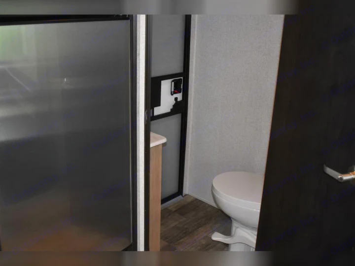RV rental interior: compact kitchen area with stainless steel refrigerator, and a glimpse into the bathroom with a white toilet.. Forest River Surveyor 2021