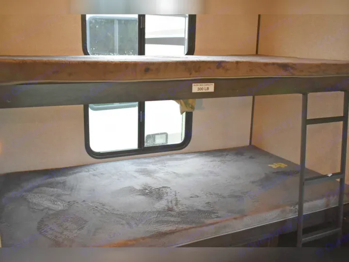 An RV rental's interior bunk beds. Two mattresses, windows, and a top bunk 300 LB capacity tag are visible.. Forest River Surveyor 2021