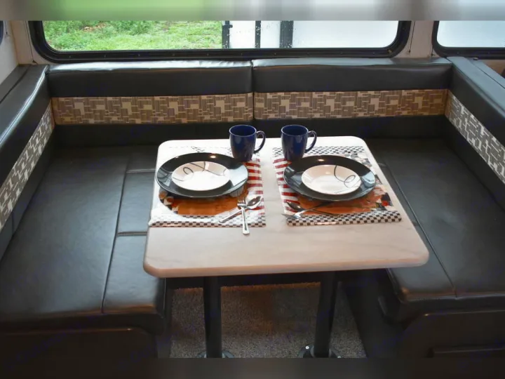 RV rental dining area with comfortable black seating and a table set for two. Ideal for meals on the road.. Forest River Surveyor 2021
