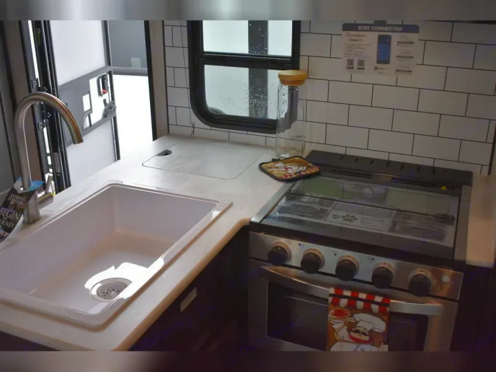 Inside an RV rental: a clean, compact kitchen with a sink, stove/oven, and tile backsplash. Ready for your travel meals.. Forest River Surveyor 2021