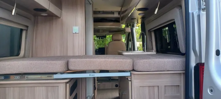 RV rental van interior with a versatile bed/seating, compact kitchen, and light wood finishes. Open rear doors.. Thor Scope 2023