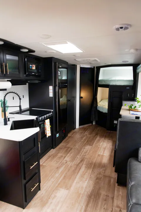 Spacious RV rental interior: modern kitchen with black cabinets & white counters, bunk beds, and dining area.. Forest River Cherokee Grey Wolf 2022
