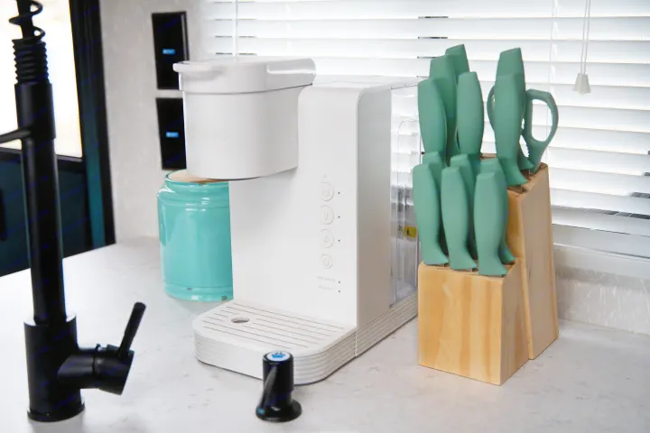 A clean RV rental kitchen counter featuring a white Keurig coffee maker, a black faucet, and a wooden block of green-handled knives.. Forest River Cherokee Grey Wolf 2022