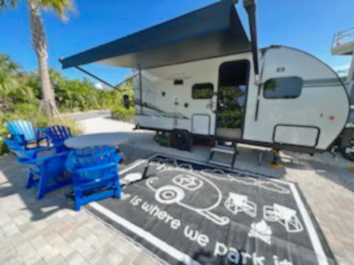 This inviting RV rental features an extended awning, blue Adirondack chairs, and a "Home is where we park it" mat, ready for a relaxing campsite stay.. Forest River Cherokee Wolf Pup Black Label 2021