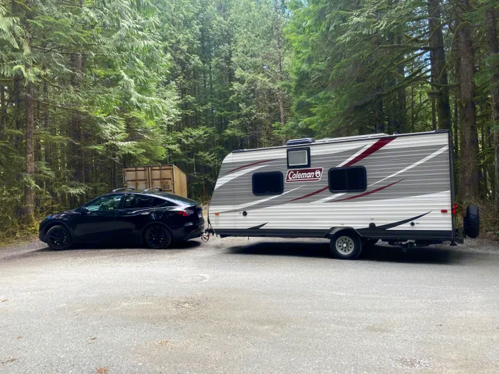 An electric Tesla Model Y tows an RV rental through a peaceful, green forest. Ready for a sustainable camping trip.. Dutchmen Coleman Lantern LT 2019