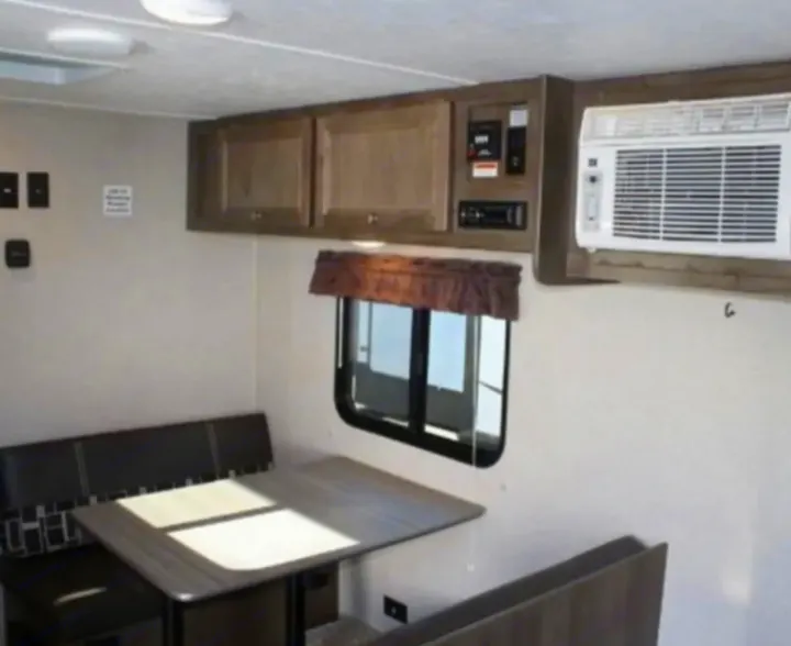 RV rental interior: A bright dinette with a table and benches, overhead cabinets, and wall-mounted AC unit offer comfortable living.. Dutchmen Coleman Lantern LT 2019