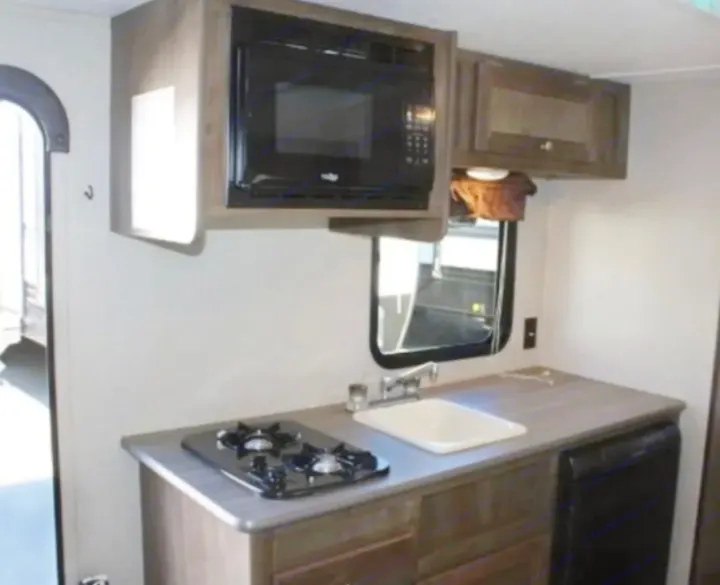 Peek inside this RV rental's practical kitchen: microwave, two-burner stove, sink, and a mini-fridge for your travels.. Dutchmen Coleman Lantern LT 2019