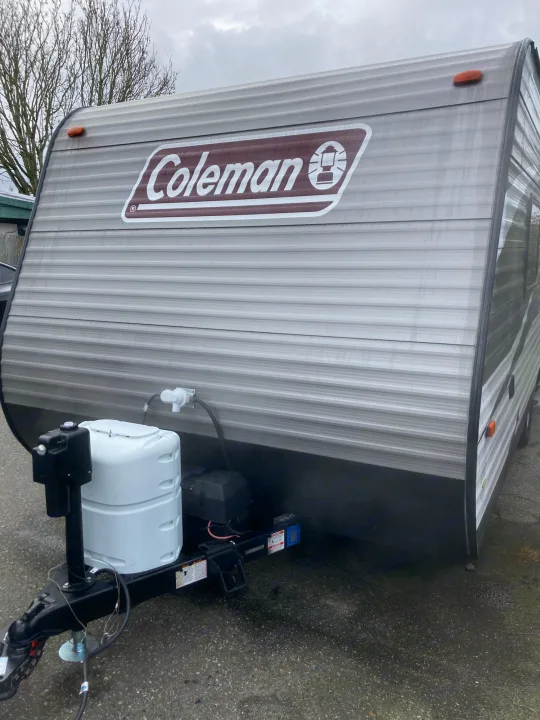 Coleman travel trailer RV rental, parked on asphalt. Features gray siding, black skirting, and front utility setup.. Dutchmen Coleman Lantern LT 2019