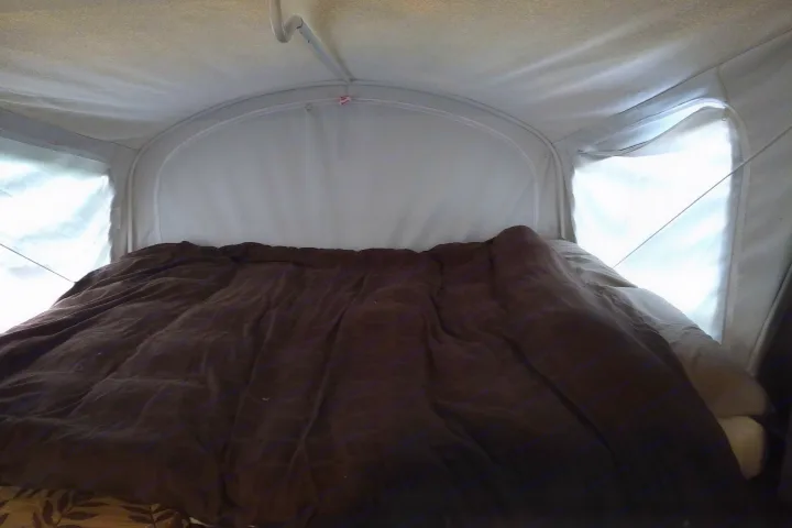 Cozy RV rental sleeping area with a dark comforter and light-filled pop-up tent windows.. Other Other 2015
