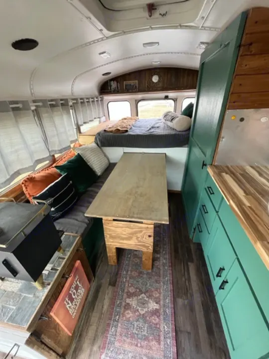 Cozy RV rental interior: compact kitchen with teal cabinets, dining table, bed, and lounge area on wood floors.. GMC Savana 2002
