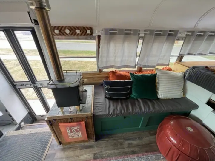 Step inside this charming RV rental: a wood stove, cozy seating, and ambient light define this unique bus conversion interior.. GMC Savana 2002