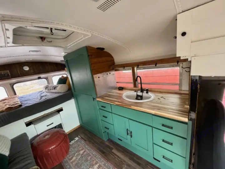 Step inside this cozy RV rental bus conversion, featuring a spacious bed and fully equipped kitchen with teal cabinets.. GMC Savana 2002