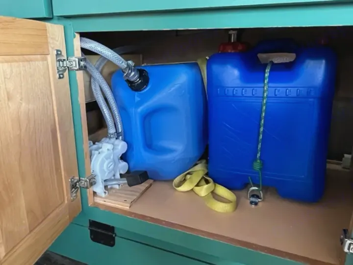 RV rental water system: Two blue tanks, pump with hoses, and tie-downs inside a cabinet for fresh water supply.. GMC Savana 2002