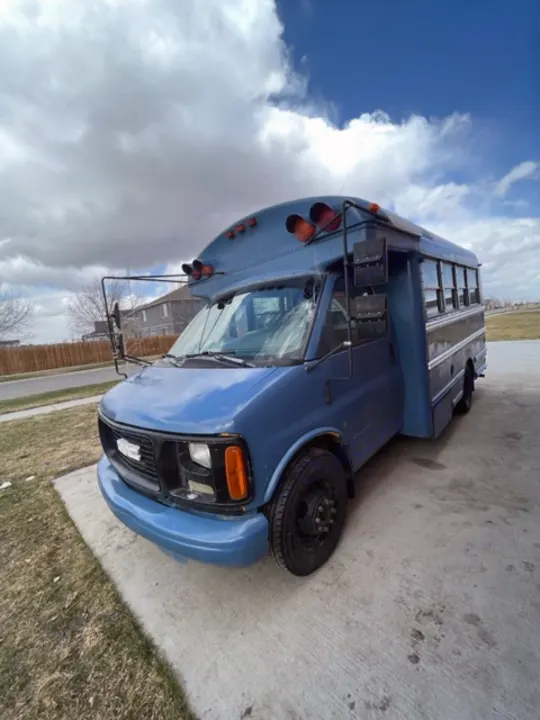 Blue converted shuttle bus RV rental, parked on concrete under a cloudy sky.. GMC Savana 2002