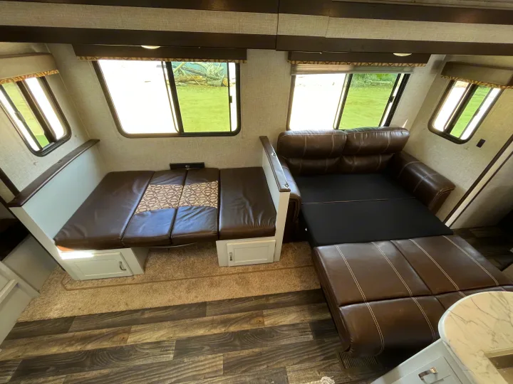 Comfortable RV rental interior featuring a convertible L-shaped sofa, dinette, and bright windows.. Keystone RV Bullet Ultra Lite 2019
