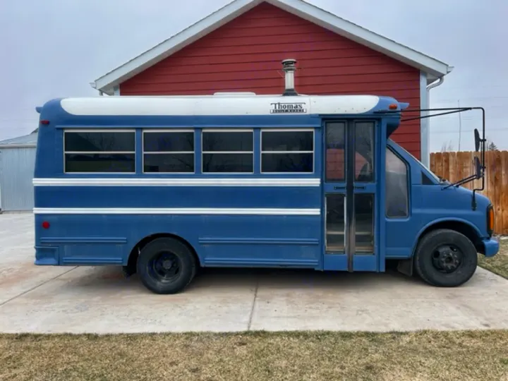 Blue Thomas school bus converted to RV, featuring a chimney & tinted windows, perfect for an rv rental.. GMC Savana 2002