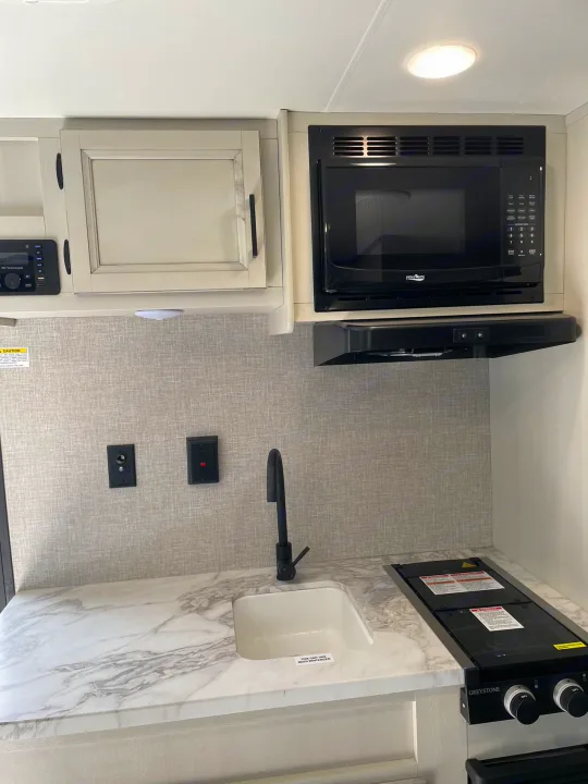 Modern RV rental kitchen with white marble counters, black appliances (sink, stove, microwave), & cabinets.. Jayco Jay Flight SLX 2022