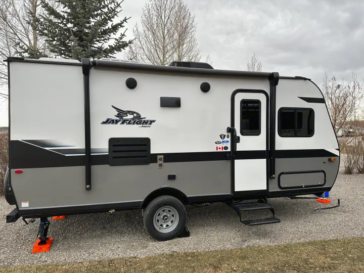Jayco Jay Flight travel trailer rv rental is set up at a gravel campsite, ready for your outdoor escape.. Jayco Jay Flight SLX 2022