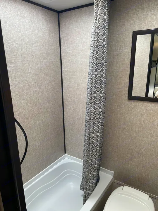 RV rental interior: A compact bathroom with white shower/tub, patterned curtain, and mirror. Light grey textured walls.. Jayco Jay Flight SLX 2022
