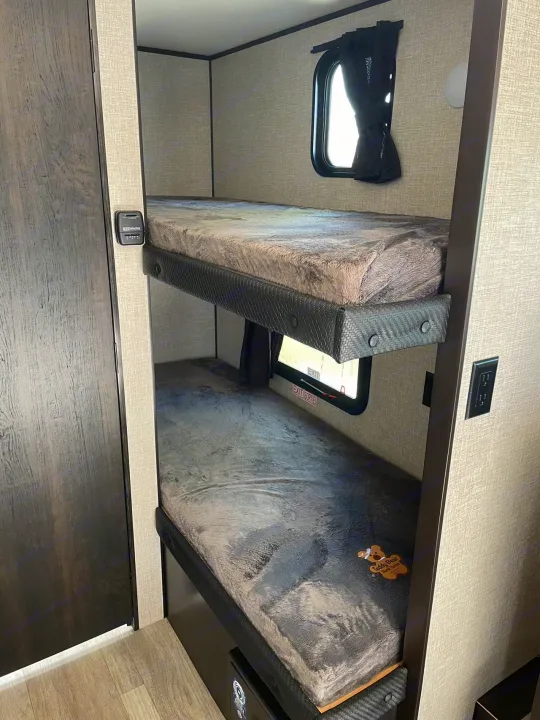 Inside an RV rental, two plush bunk beds with soft gray bedding and individual windows are visible, ready for comfortable stays.. Jayco Jay Flight SLX 2022