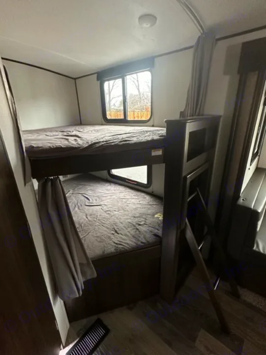 Inside an RV rental: view of sturdy bunk beds, a window, and a compact living area for travelers.. Keystone RV Springdale 2021