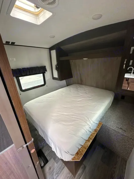 Modern RV rental bedroom interior with clean, wrapped mattress, dark wood cabinets & floor. Ready for travel.. Keystone RV Springdale 2021
