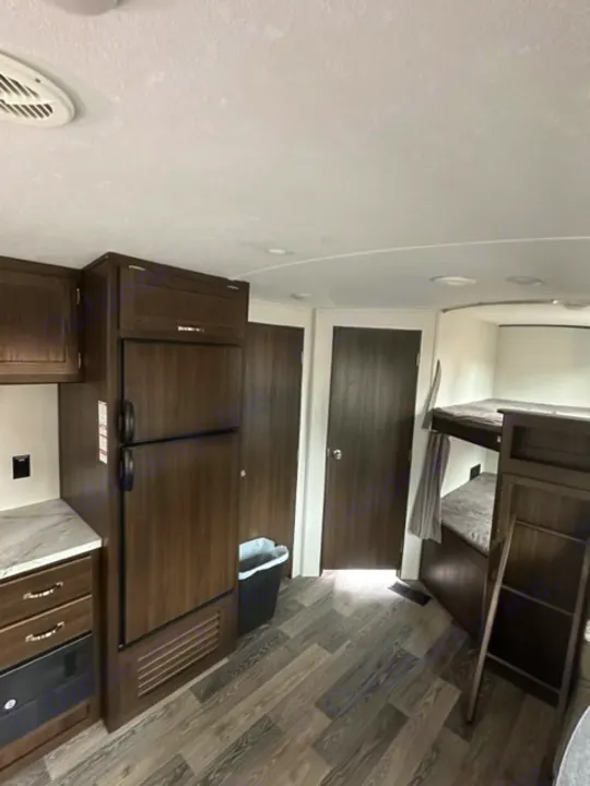 Inside this modern rv rental: dark wood kitchenette, storage, and bed area with sleek flooring.. Keystone RV Springdale 2021